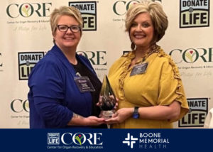 Two women are smiling and holding an award in front of a backdrop featuring 'Donate Life' and logos for CORE and Boone Memorial Health.