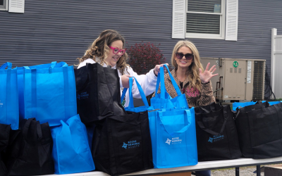 Two female volunteers hand out blue BMH tote bags with meals at the BMH 4th Annual Community Drive-Thru Thanksgiving Dinner