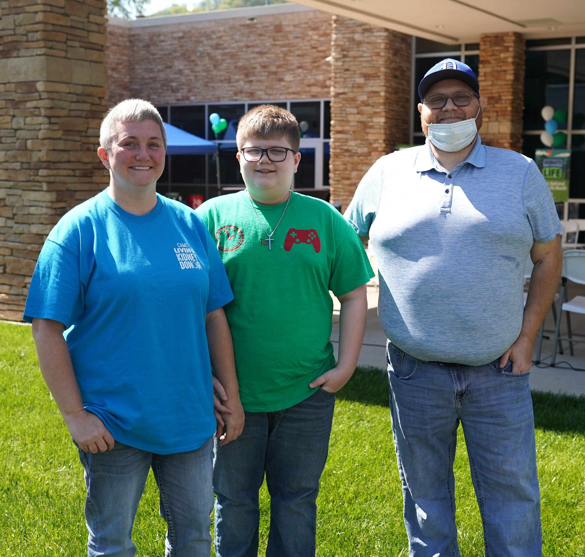 Three people—a woman, a boy, and a man—stand together outdoors on a lawn in front of Boone Memorial Hospital at Donate Life Flag Raising Ceremony