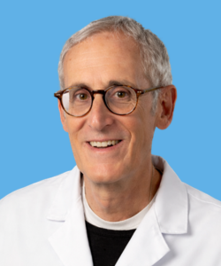 Portrait of eye surgeon Dr. Stephen Cassis wearing a white medical coat, smiling against a light blue background.